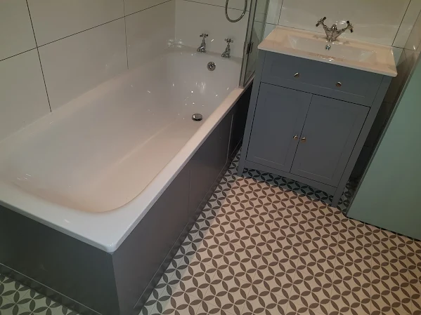 Finished bathroom with grey panelled bath, patterned floor tiles and grey vanity unit